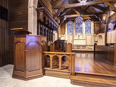 A wooden pulpit and beautiful wood church furniture with stained glass in the background at the Christ of the Redeemer Church in Longport, New Jersey.