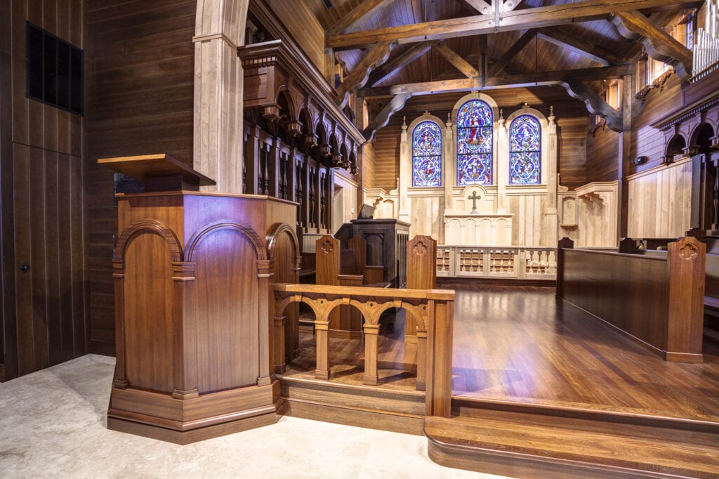 A wooden pulpit and beautiful wood church furniture with stained glass in the background at the Christ of the Redeemer Church in Longport, New Jersey.