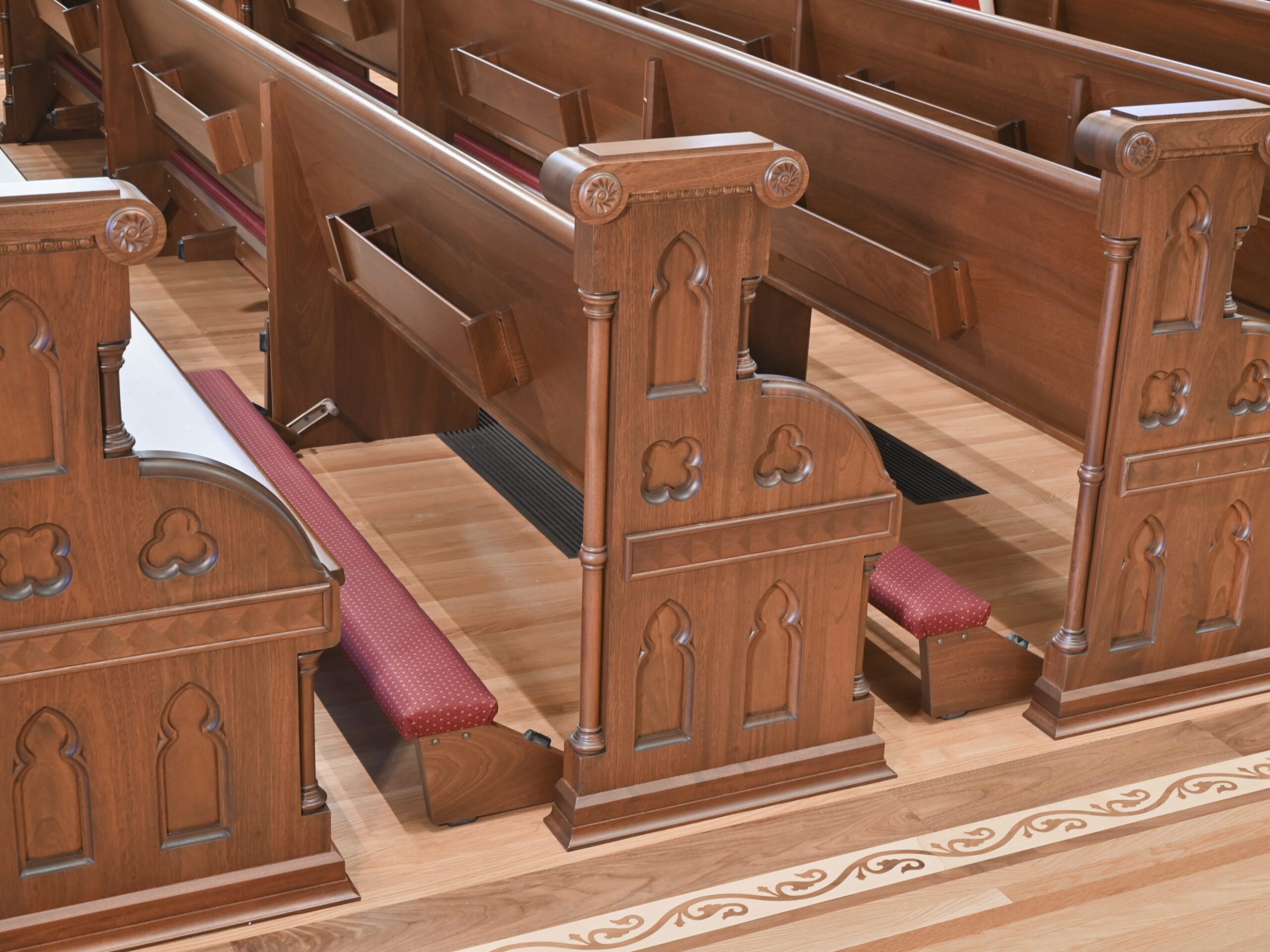 Richly inlaid pews with red kneelers on hinges at the back