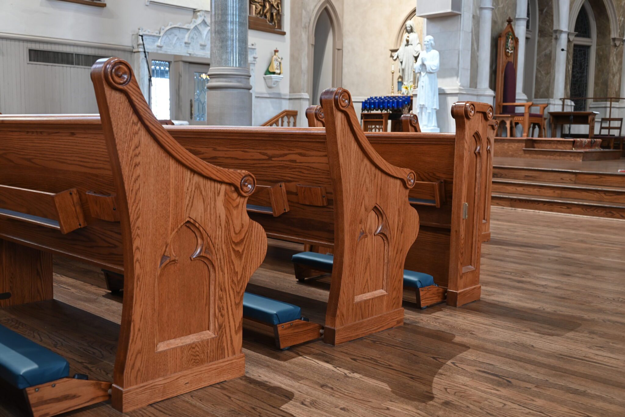 A back view of the front four rows of pews, with fancifully curved end-caps and blue kneelers.