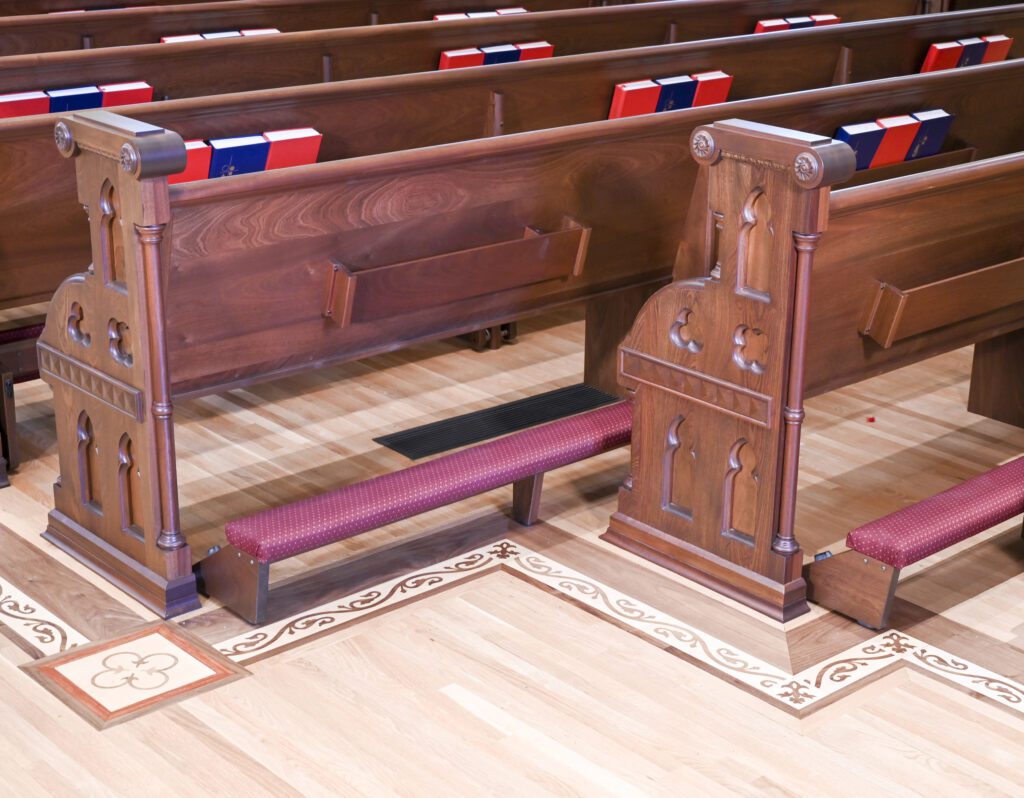 Church pews with ornate pew ends and padded church kneelers in front of them.