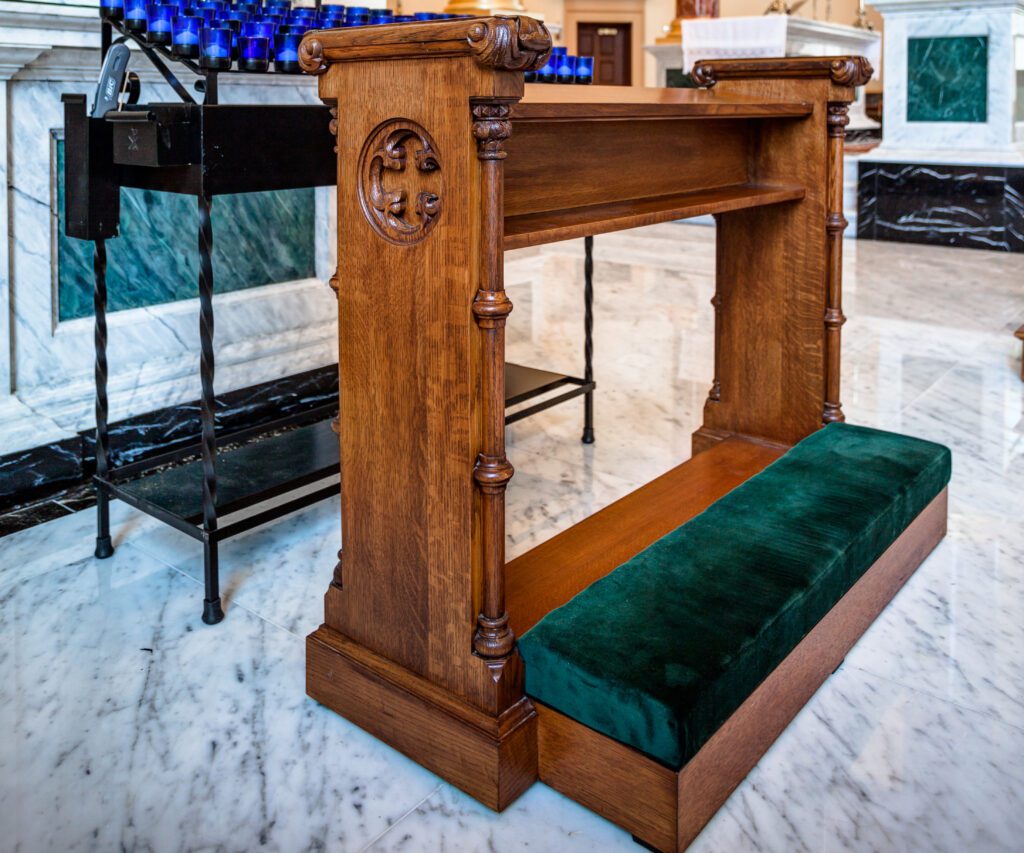 A votive stand at a church with a single altar rail and a catholic kneeler in front of it.